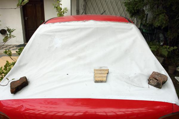 auto cubierto estacionado, baldosas rotas, lona blanca